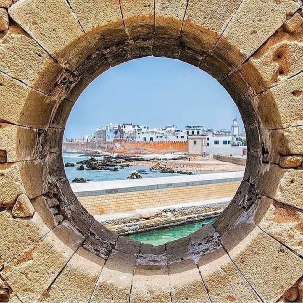 View of Essaouira’s fortified medina through a circular stone window, showing the Atlantic coastline