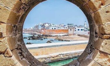 View of Essaouira’s fortified medina through a circular stone window, showing the Atlantic coastline