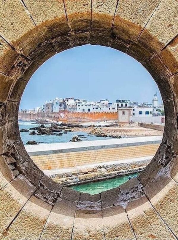 View of Essaouira’s fortified medina through a circular stone window, showing the Atlantic coastline