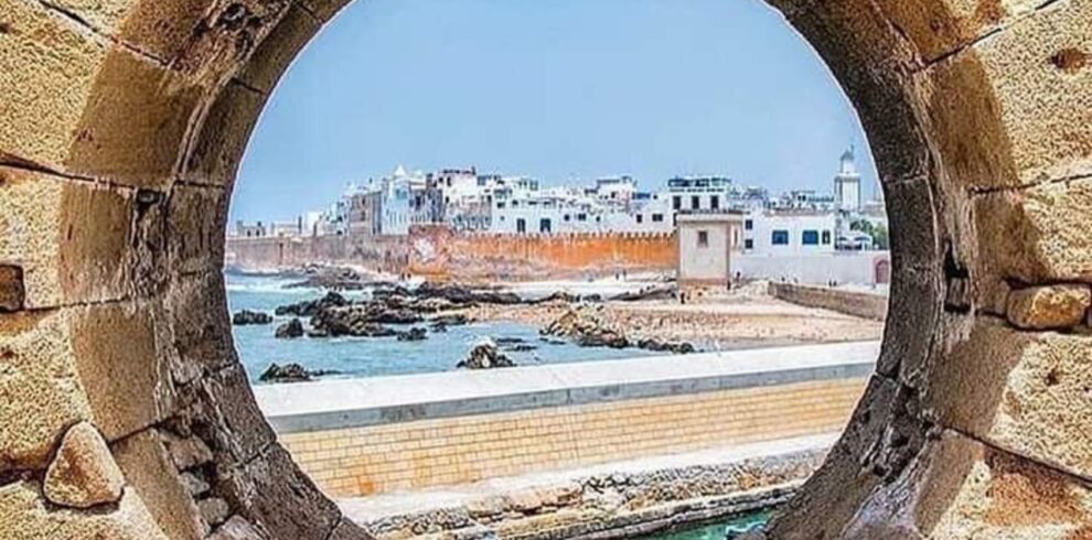 View of Essaouira’s fortified medina through a circular stone window, showing the Atlantic coastline