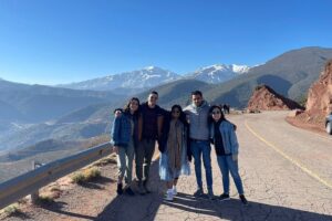 Group of travelers posing on a scenic mountain road with snow-capped peaks in the background