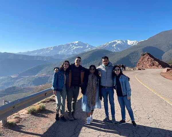 Group of travelers posing on a scenic mountain road with snow-capped peaks in the background