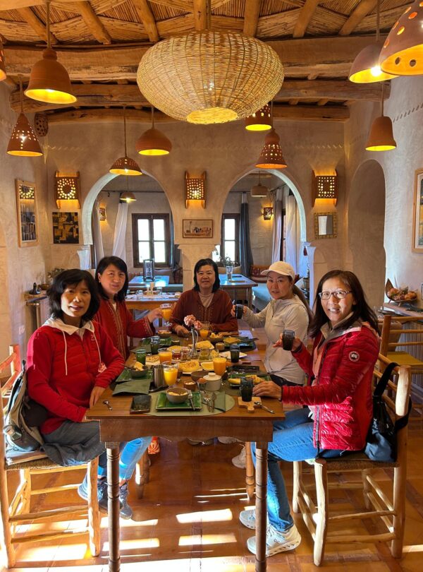 Group of travelers enjoying breakfast in a traditional Moroccan riad with rustic decor and warm lighting