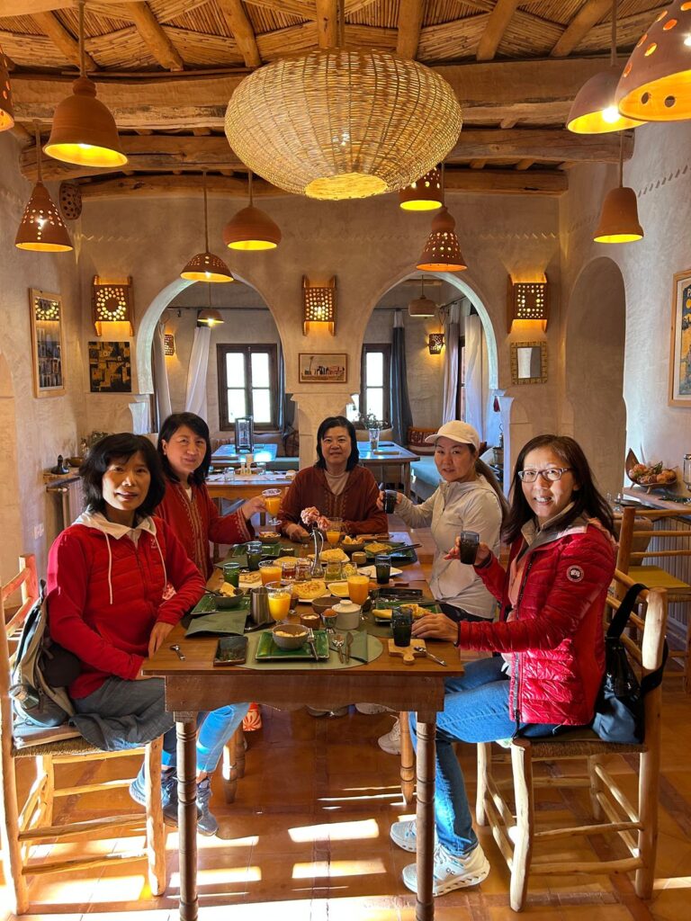 Group of travelers enjoying breakfast in a traditional Moroccan riad with rustic decor and warm lighting